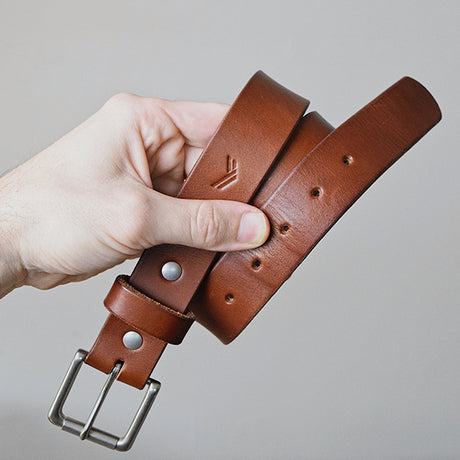 A hand holds a stylish brown leather belt with a silver buckle, showcasing its smooth texture and adjustable holes.